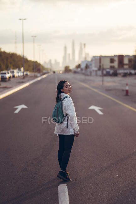 Rückansicht einer Reisenden, die eine Allee mit Dubai Marina im Hintergrund hinuntergeht — Stockfoto