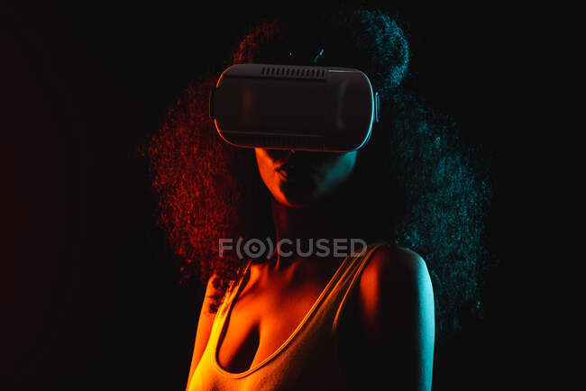 Анонимная этническая женщина исследует виртуальную реальность в наушниках на черном фоне — стоковое фото