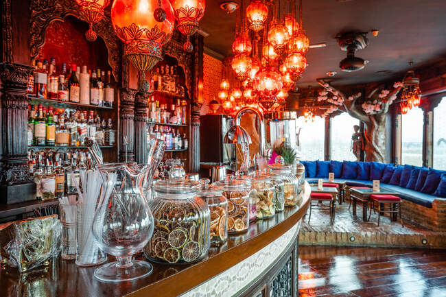 Interior de acogedor pub con lámparas iluminadas y mostrador de madera con decoraciones variadas - foto de stock