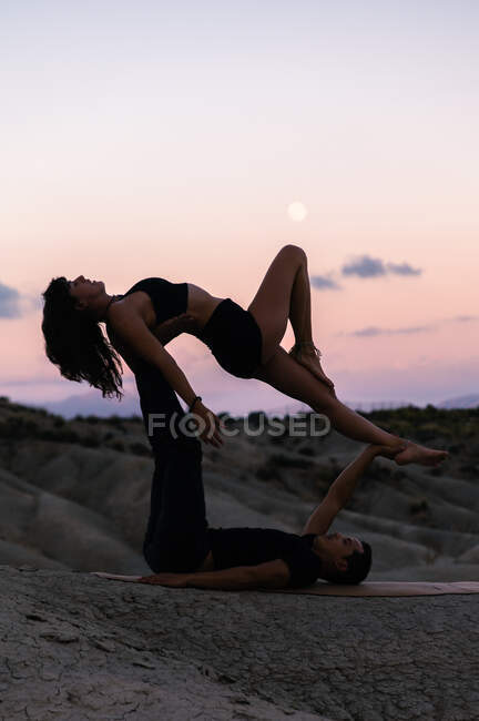 Side view of graceful couple doing acroyga on background of sunset sky in mountains — Stock Photo