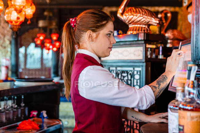 Vista laterale del barista femminile utilizzando cashbox e toccando schermo di visualizzazione mentre si lavora in bar — Foto stock