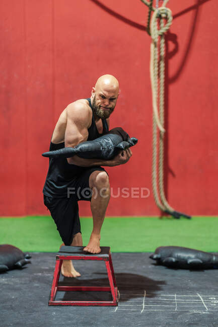 Powerful sportsman with heavy bag stepping and lunging on stool during functional training in modern gym — Stock Photo