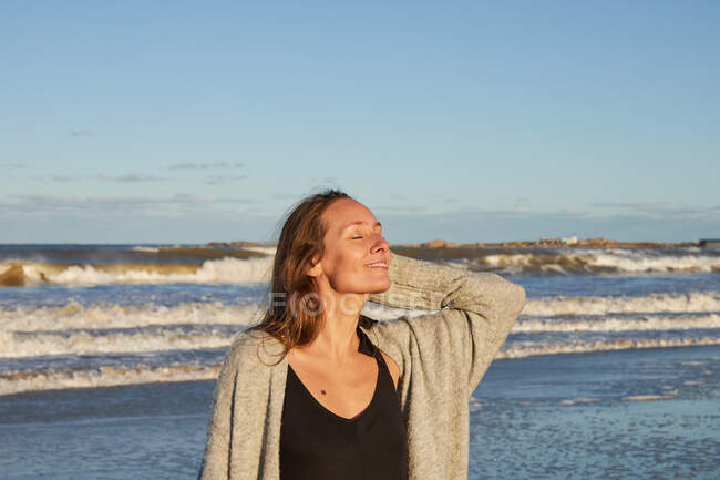 Tranquilo fêmea com olhos fechados desfrutando do pôr do sol no verão na praia perto do mar — Fotografia de Stock