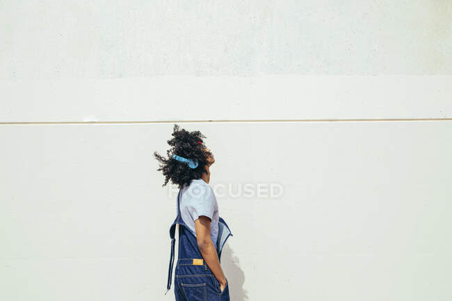Vue latérale d'un jeune homme ethnique réfléchi en tenue rétro avec des cheveux bouclés regardant vers le haut sur fond de mur en béton — Photo de stock