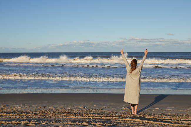 Обратный вид на неузнаваемую женщину, наслаждающуюся свободой с поднятыми руками, стоя летом на берегу моря — стоковое фото
