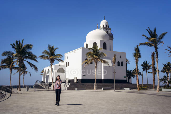 Giovane turista donna in piedi sulla piazza lastricata contro il bellissimo edificio bianco della moschea dell'isola con cielo azzurro chiaro sullo sfondo nella giornata di sole a Gedda in Arabia Saudita — Foto stock