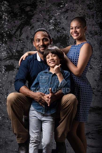 Stilvolles multirassisches Paar mit Teenager-Sohn, das im Studio auf dunklen Hintergrund in die Kamera blickt — Stockfoto