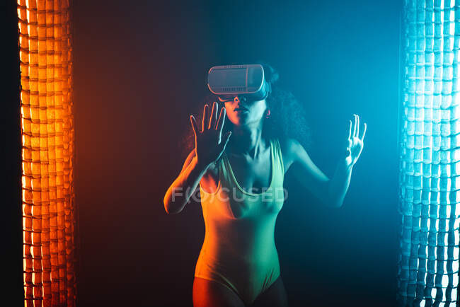 Anonyme verblüffte ethnische Frau mit offenem Mund erkundet virtuelle Realität im Headset auf schwarzem Hintergrund — Stockfoto
