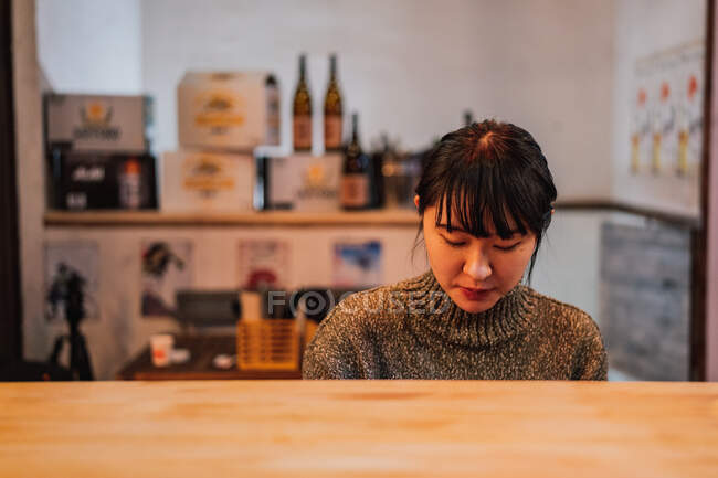 Conteúdo Mulher asiática em camisola casual olhando para baixo enquanto se senta na mesa de madeira no bar ramen — Fotografia de Stock