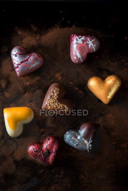 Верхний вид композиции с разноцветными шоколадными конфетками ручной работы в форме сердца на деревянном столе — стоковое фото