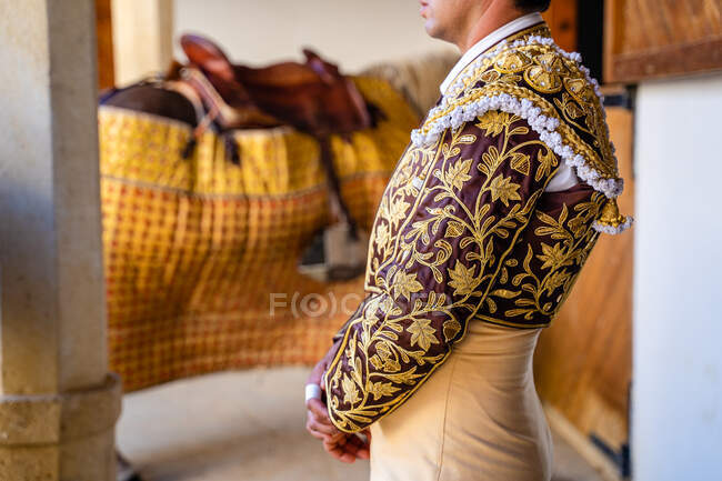 Vue latérale du matador dans les vêtements ornementaux traditionnels avec broderie debout dans la grange avant la performance corrida — Photo de stock