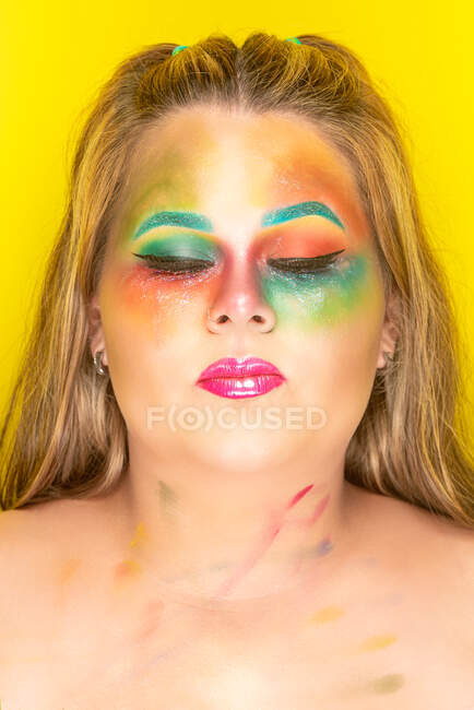 Plus size femminile con brillante trucco colorato occhi chiusi contro sfondo giallo — Foto stock