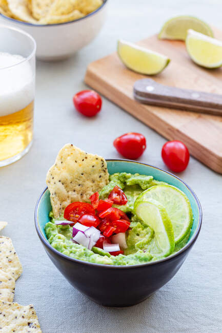 High angle of bowl with tasty guacamole with ripe cherry tomato and red onion near lime slices — Stock Photo
