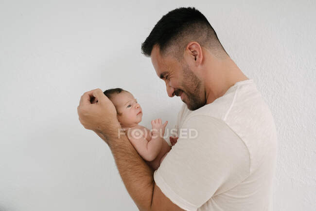 Gentile padre in piedi con bambino sveglio vicino al muro in camera a casa — Foto stock