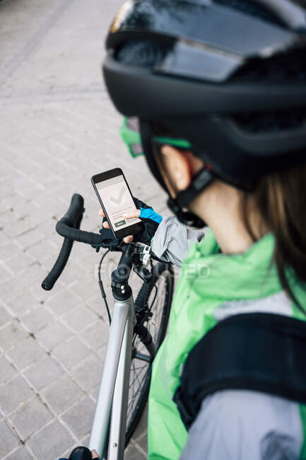 Сверху анонимный курьер осматривает маршрут на карте GPS, прежде чем проехать на велосипеде по городской улице — стоковое фото