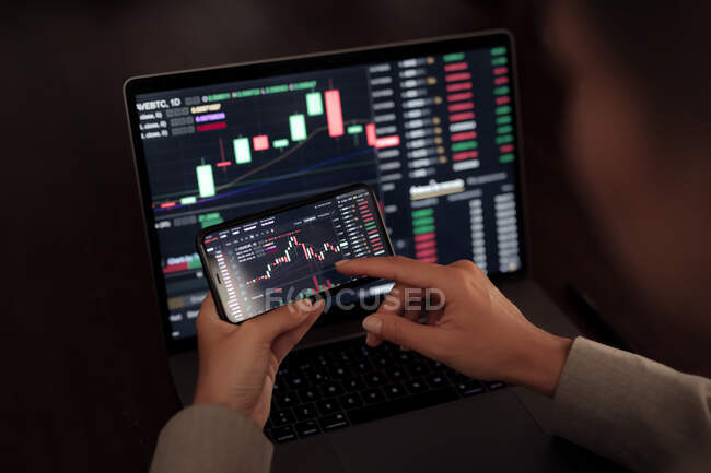Corretor de culturas sem rosto usando telefone celular enquanto trabalhava com gráfico financeiro durante a negociação — Fotografia de Stock