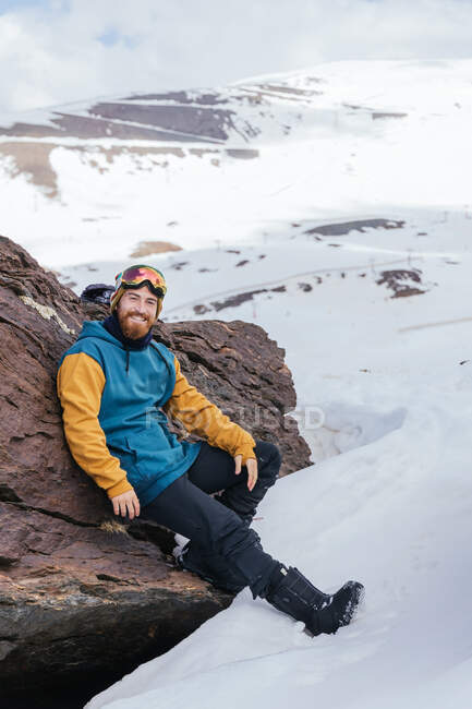 Athlète masculin barbu souriant en vêtements de sport regardant la caméra alors qu'il était assis sur le mont en saison hivernale en Espagne — Photo de stock