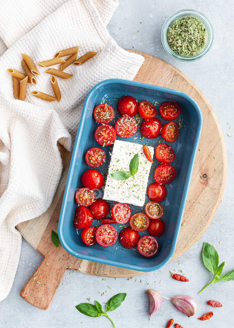 Vista dall'alto di pomodorini maturi con fette di olive nere e formaggio feta in teglia vicino penne crude — Foto stock