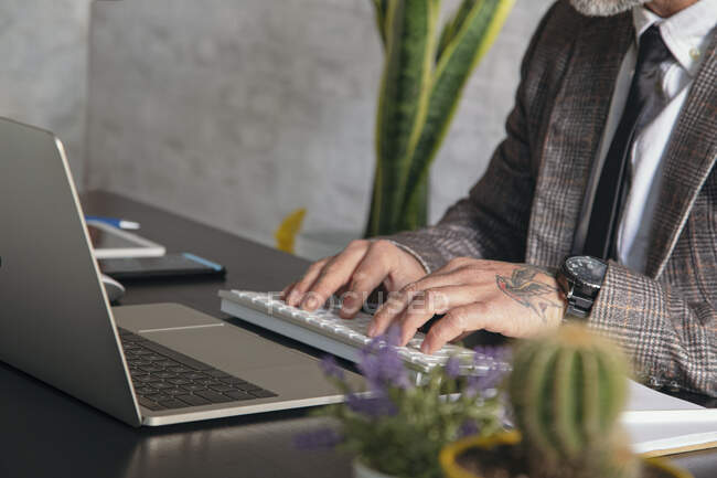 Ritagliato imprenditore maschio di mezza età irriconoscibile in abbigliamento formale che lavora su laptop a tavola in ufficio — Foto stock