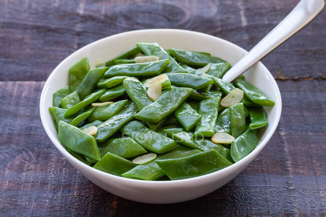 Von oben gesunder Salat mit grünen Bohnen und Knoblauchscheiben in Schüssel auf Holztisch serviert — Stockfoto