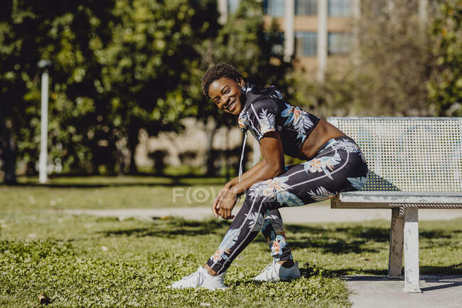 Молодая фитнес афроамериканка отдыхает после тренировки на скамейке в парке — стоковое фото