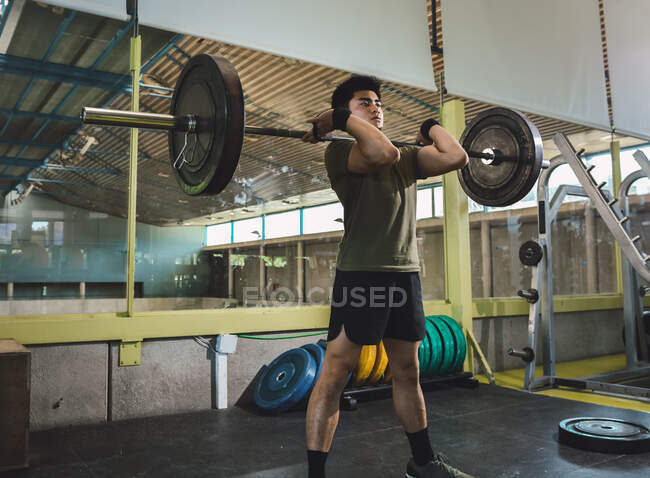 Сосредоточенный азиатский спортсмен, занимающийся тяжелой атлетикой во время тренировки в тренажерном зале — стоковое фото