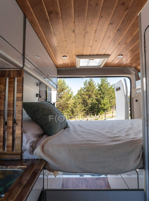 Weiches Bett mit Kissen und Decke im modernen Wohnwagen im Wald an sonnigen Tagen — Stockfoto