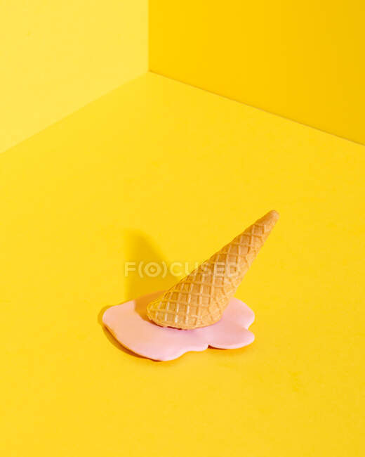 Helado de fusión rosa burlón en cono de gofre colocado sobre fondo amarillo que representa el concepto de verano - foto de stock