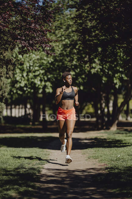 Joven fitness mujer afroamericana corriendo y haciendo ejercicio en el parque - foto de stock