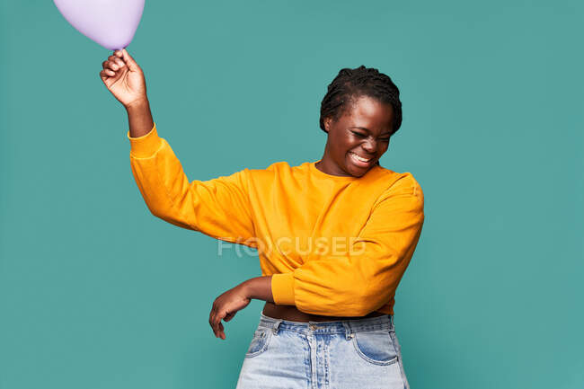 Захоплена афро-американка в джинсах і жовтий топ стоять біля падаючих повітряних куль на синьому тлі в студії — стокове фото