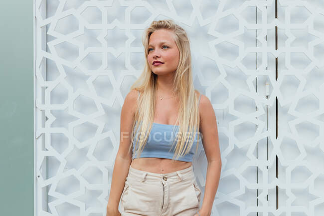 Delighted female in trendy crop top and with long blond hair standing in city street and looking away — Stock Photo