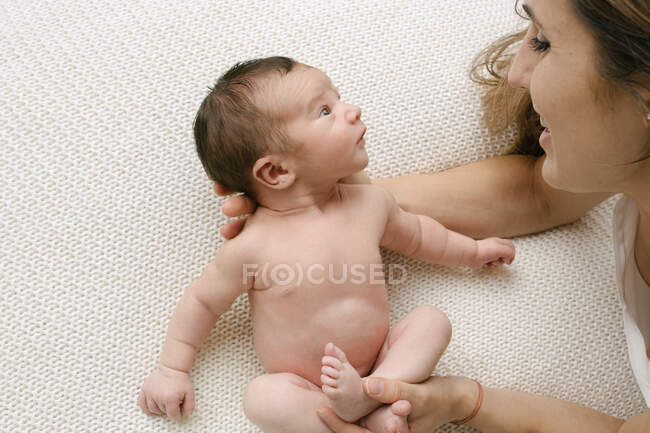 Сверху обрезанная неузнаваемая любящая мать смотрит на очаровательного обнаженного младенца в постели дома — стоковое фото