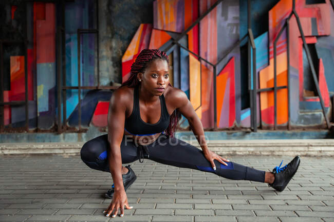 Молода афро-американська спортсменка, що займається м'язовими видами, розтягує ногу на вулиці. — стокове фото