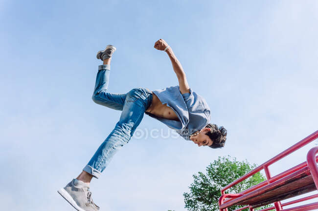 Basso angolo impavido giovane uomo saltare sopra ringhiera metallica in città durante l'esecuzione di acrobazia parkour nella giornata di sole — Foto stock