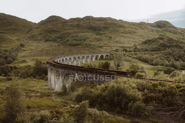 Стара залізнична колія вздовж стародавнього арочного мосту біля гори Хілл у сірий день у Гленфіннані, сільській місцевості Великої Британії. — стокове фото