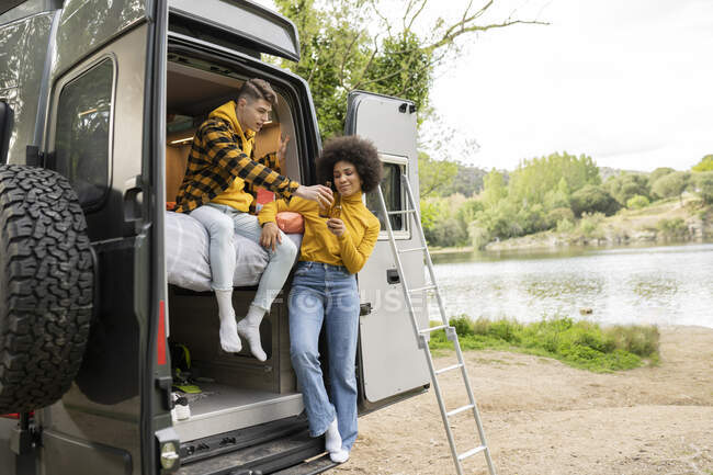 Happy black woman with beer toasting and smiling standing in van with boyfriend during road trip in countryside — Stock Photo