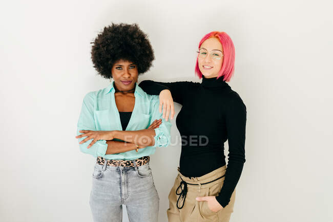 Весела молода рожева жінка і афроамериканська дівчина в стильному одязі, розважаючись разом на білому фоні. — стокове фото