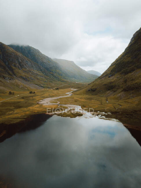 Ciel couvert au-dessus des collines se reflétant dans un lac aux eaux calmes dans la campagne britannique. — Photo de stock