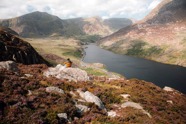 Vista posteriore di anonime donne che ammirano colline e fiume mentre siedono su un pendio accidentato durante il viaggio attraverso Snowdonia, nella campagna del Regno Unito — Foto stock