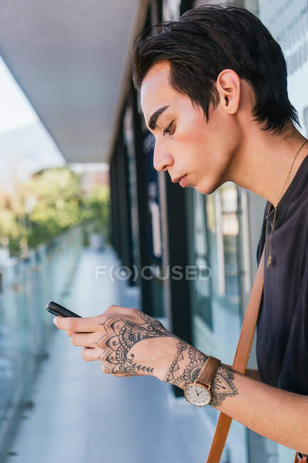 Side view of serious gay male messaging on social media on mobile phone while standing in street — Stock Photo