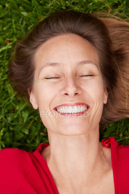 Mulher com os olhos fechados vestidos de vermelho deitado no chão em um parque com grama — Fotografia de Stock