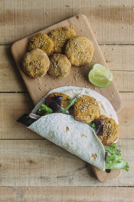 Top view of tasty sweet potato falafel and fresh lettuce wrapped in tortilla and placed near lime on cutting board on lumber timber — Stock Photo