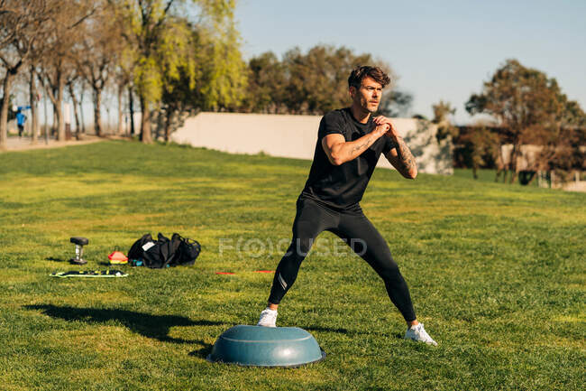Adult male athlete in sports clothes working out with clasped hands while looking away on lawn — Stock Photo