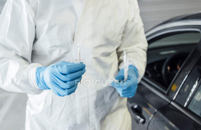 Biólogo con guantes protectores que realiza una prueba de coronavirus en una persona en un coche - foto de stock
