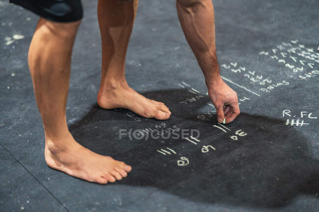 Unrecognizable barefoot sportsman making notes with chalk on floor during intense workout in gym — Stock Photo