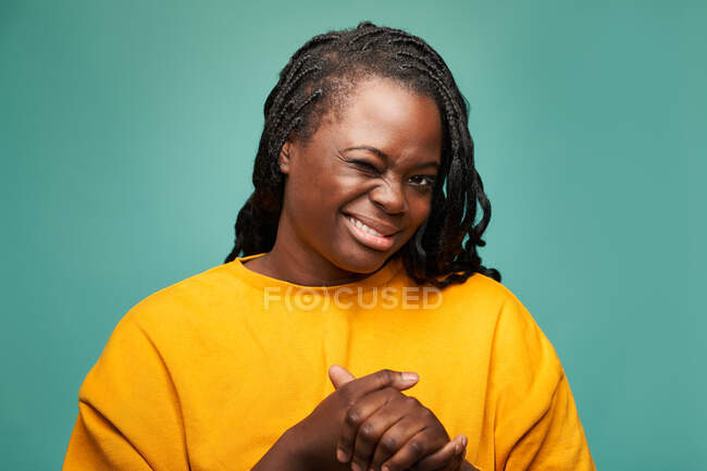 Frohe Afroamerikanerin in gelben Kleidern zwinkert in die Kamera vor blauem Hintergrund — Stockfoto