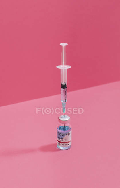 Fiole de vaccin contre le coronavirus près de la seringue avec aiguille sur fond rose — Photo de stock