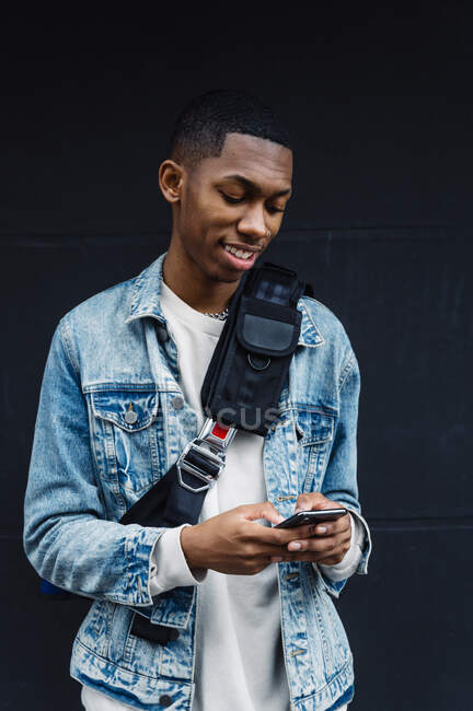 Frontansicht eines jungen schwarzen Mannes mit Handy und Rucksack auf der Straße — Stockfoto