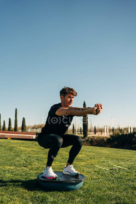 Atleta maschio determinato con tatuaggi e braccia aperte che si allena sulla filatrice mentre guarda avanti in città — Foto stock
