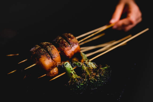 Mão segurando deliciosos espetos picantes cozidos com carne e brócolis saudável — Fotografia de Stock